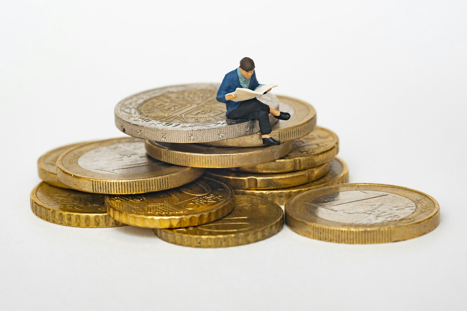 Pilha de moedas com miniatura de pessoa lendo jornal